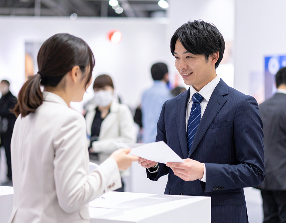 大型の展示会会場でチラシを配るコンパニオン